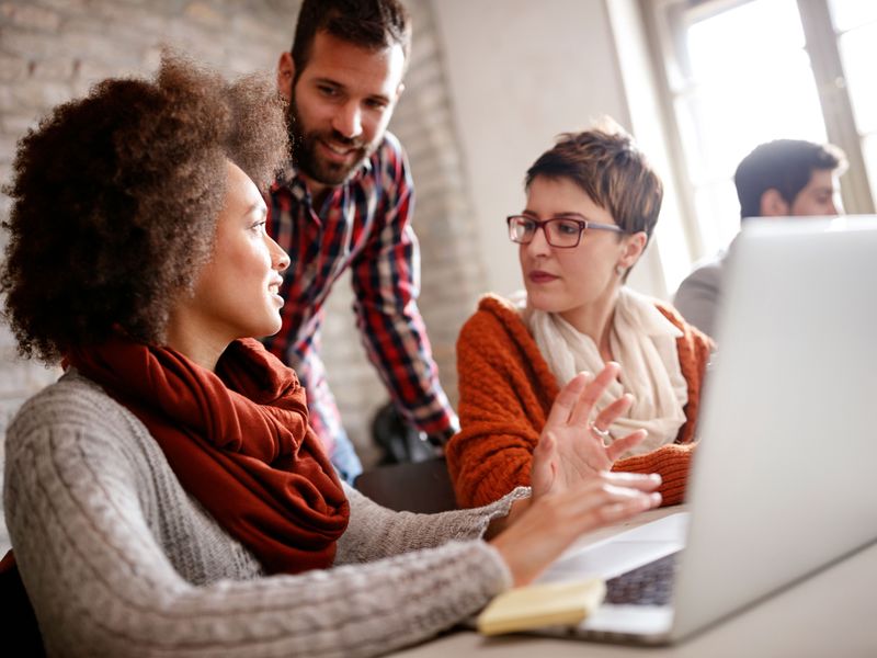 Teilnehmerinnen und Teilnehmer der Werbe Akademie lernen und arbeiten gemeinsam vor einem Laptop