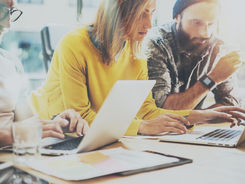 Teilnehmerinnen und Teilnehmer der Werbe Akademie lernen und arbeiten gemeinsam vor einem Laptop